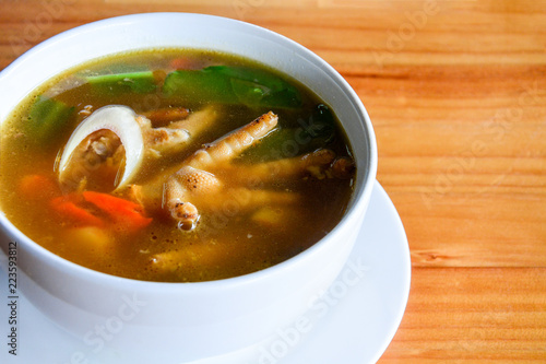 spicy and sour chicken feet soup (Tom Yum) in white ceramic bowl on wooden table background, copy space