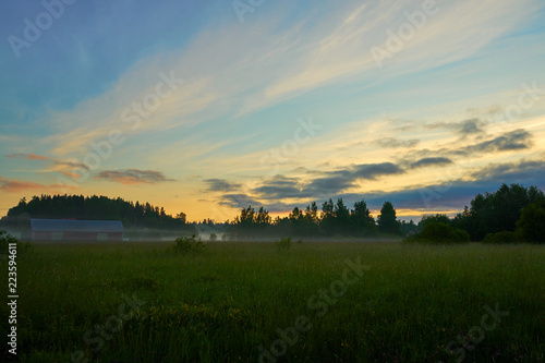 Foggy sunrise on a field with cloudy sky.