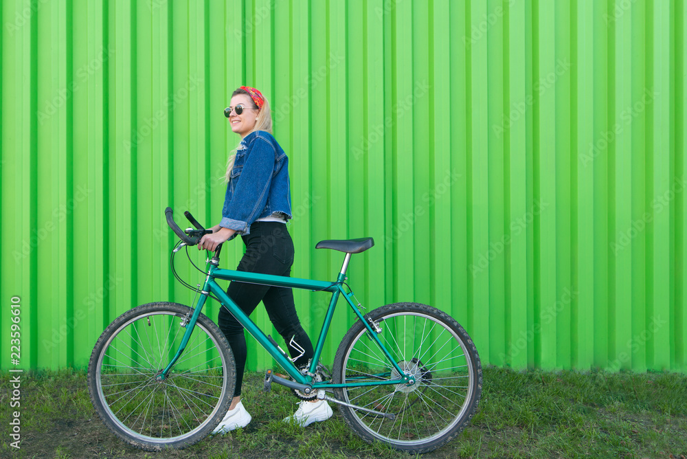 Portrait of a stylish woman in full length pulling a bicycle on the background of a green wall. Teen girl walking with a bicycle on a green background. Copyspace Portrait of a stylish woman in full length pulling a bicycle on the background of a green wall. Teen girl walking with a bicycle on a green background. Copyspace
