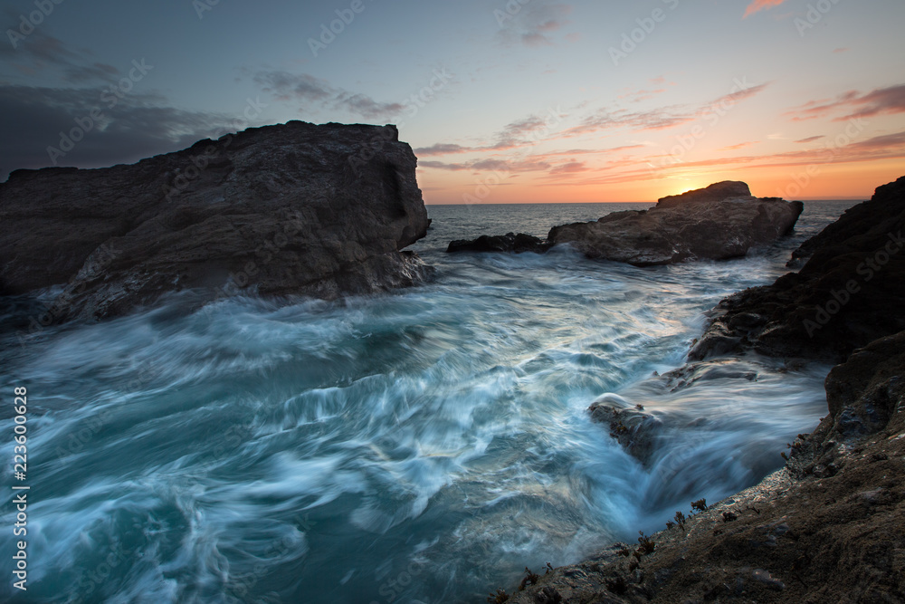 A long exposure of blurred waves swirling and crashing over rugged rocks on the rocky Cornish coastline in Cornwall, UK.