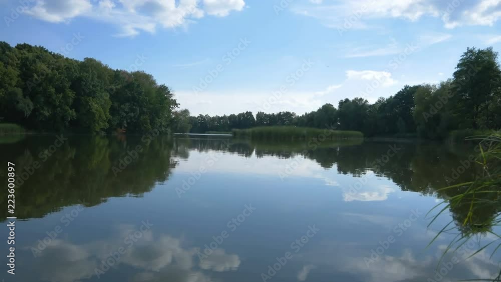 View of the river with reeds along the banks of which there are many trees. TimeLapse video. The sky is reflected in the water.