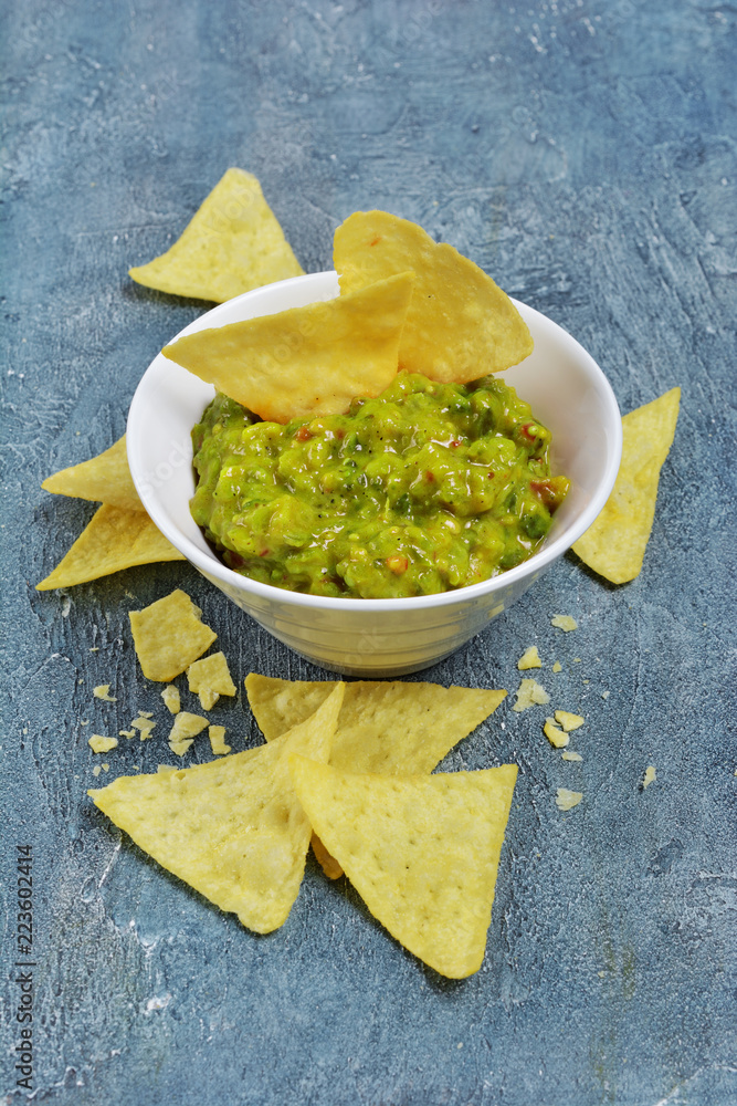 Mexican nachos chips with green guacamole sauce or dip in white bowl Mexican nachos chips with green guacamole sauce or dip in white bowl
