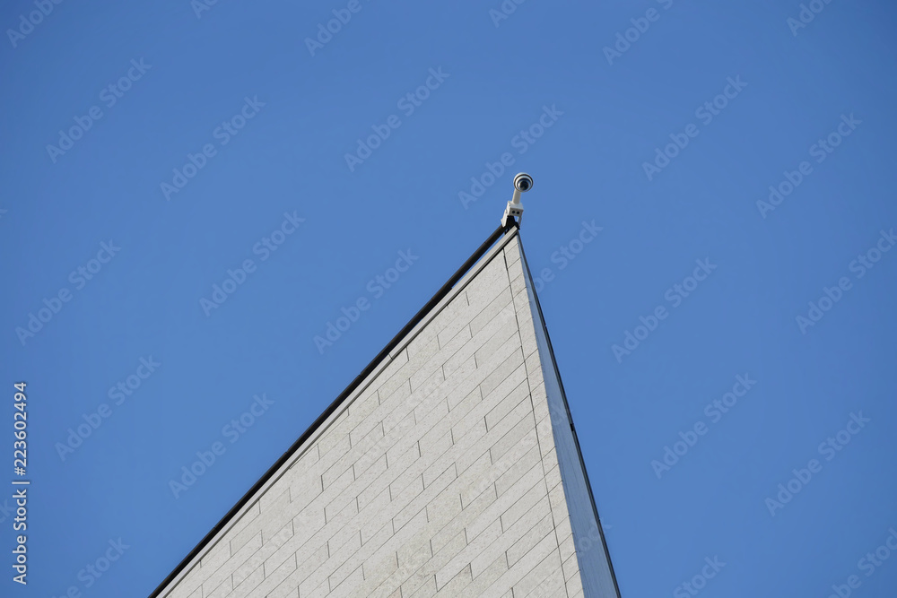 Security camera at the top of a new building with blue sky in background Security camera at the top of a new building with blue sky in background