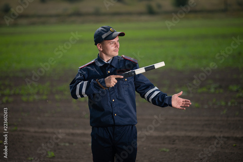 policeman in uniform with a rod in his hand on the background of rural landscape