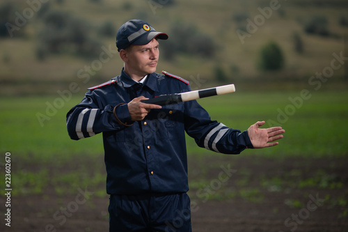 policeman in uniform with a rod in his hand on the background of rural landscape