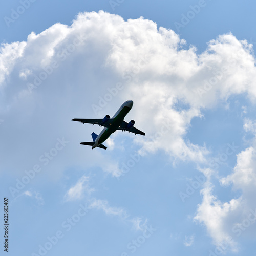 Passenger airplane flying against white clouds and blue sky.