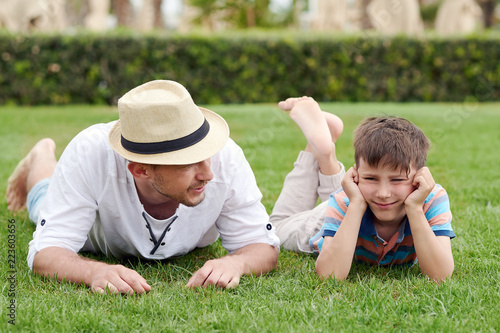 European man is laying at the hotels lawn with his cute son. They are talking and having a rest.