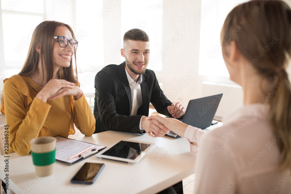 Cheerful business man with laptop and business woman in eyeglasses happily talking with applicant about work. Young employers spending job interview in office Cheerful business man with laptop and business woman in eyeglasses happily talking with applicant about work. Young employers spending job interview in office