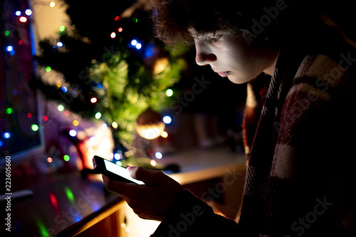 young teenage boy using the smartphone on the christmas night at home near the tree f