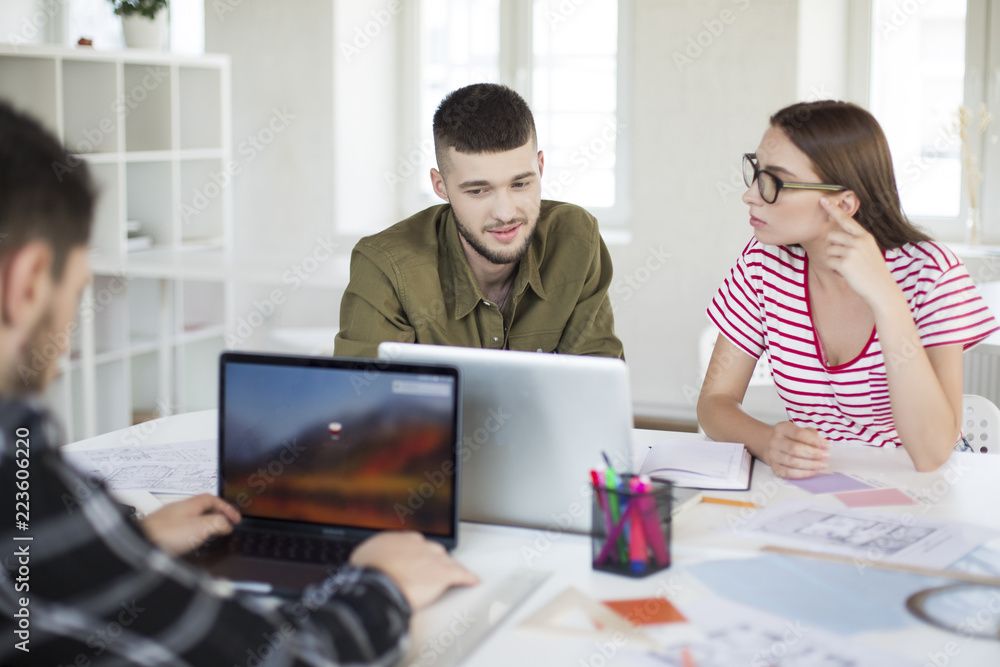 Young man in shirt and woman in striped t-shirt and eyeglasses working together with laptop. Group of cool guys spending time in office Young man in shirt and woman in striped t-shirt and eyeglasses working together with laptop. Group of cool guys spending time in office