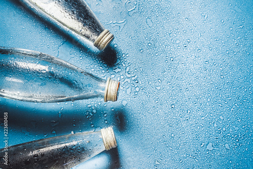 A glass bottle of water on blue background splashes drops of water on top. Quench thirst. Background water drops place for text copy space