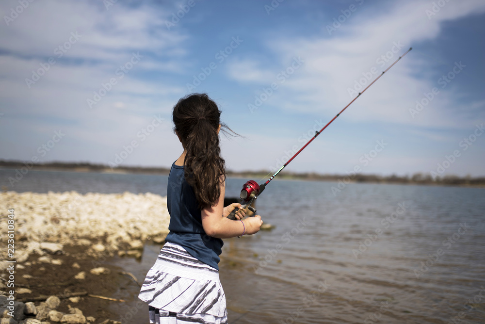 Girl in ponytail fishing in lake against cloudy sky Girl in ponytail fishing in lake against cloudy sky