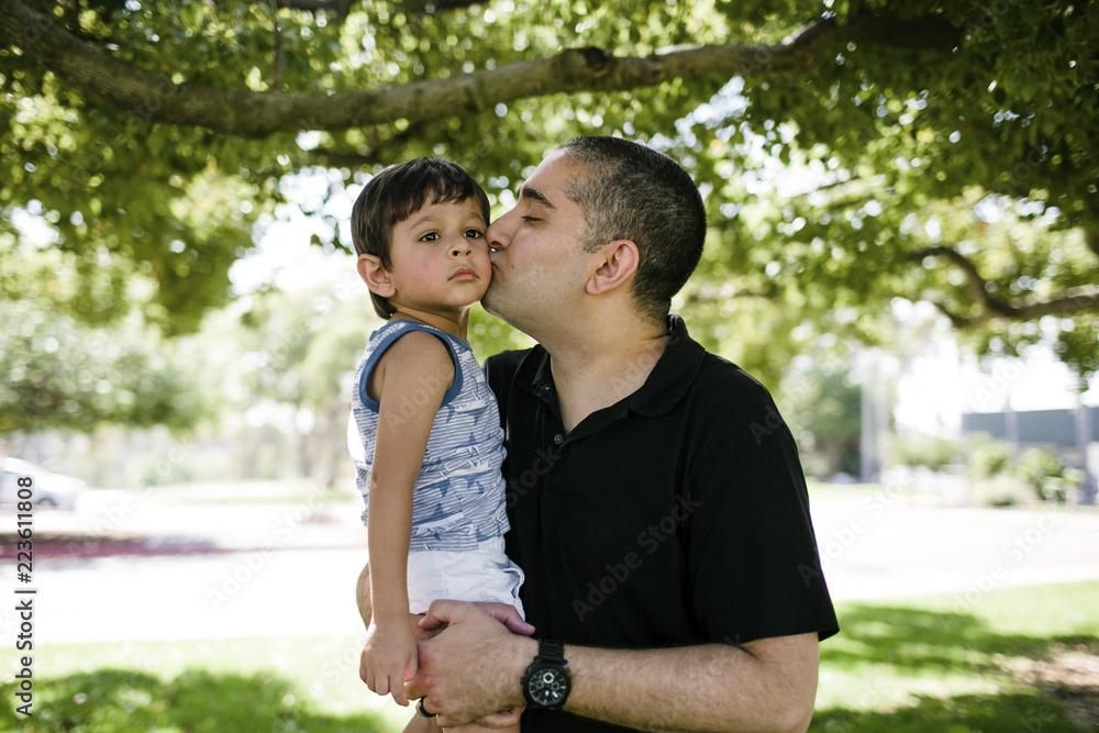 Father kissing cute son while standing at park Father kissing cute son while standing at park