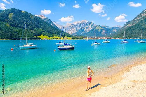 Young woman tourist standing on beautiful Achensee lake beach on sunny summer day  Tirol  Austria