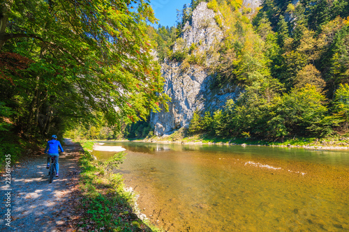 Woman cyclist riding along Dunajec river in autumn landscape of Pieniny Mountains, Poland photo