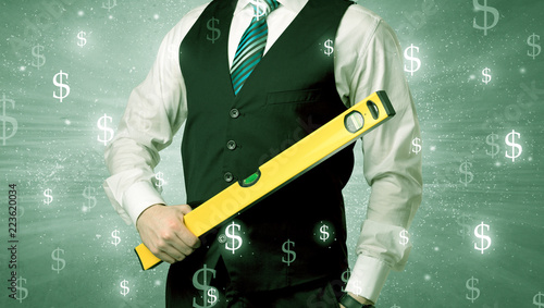 Fototapeta Naklejka Na Ścianę i Meble -  Handsome businessman holding tool with dollar symbols around and with green background