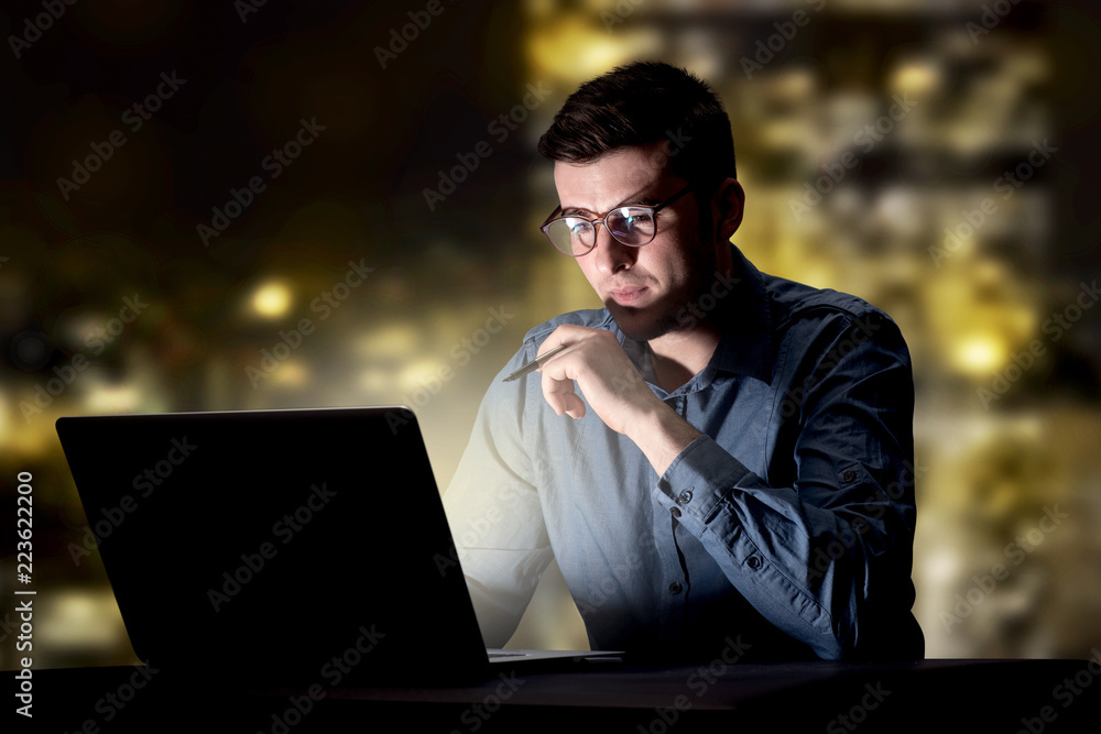 Young handsome businessman working late at night in the office with city lights in the background Young handsome businessman working late at night in the office with city lights in the background