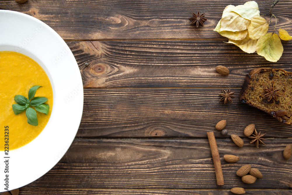 Tasty pumpkin cream soup, blended with spice and onion. Copy space, top view. Autumn mood, yellow leaves and carrot cake. Brown rustic wooden background. Tasty pumpkin cream soup, blended with spice and onion. Copy space, top view. Autumn mood, yellow leaves and carrot cake. Brown rustic wooden background.