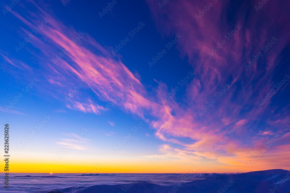 Amazing colorful sunset in mountains with absract wing shapes of clouds