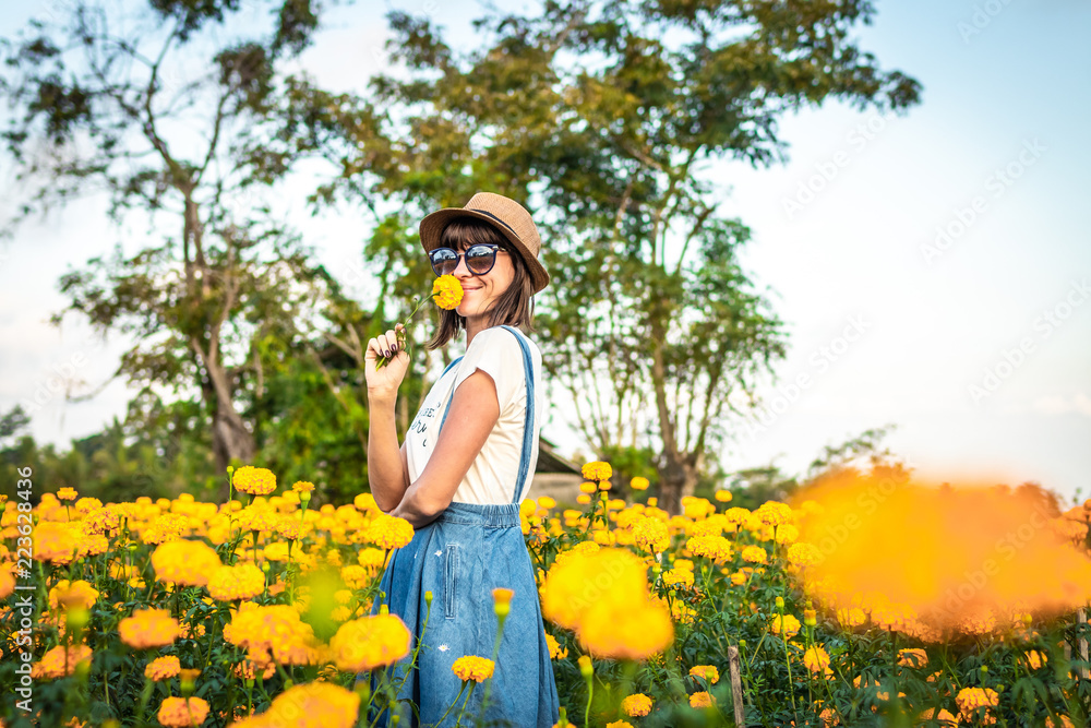 Close up portrait of happy and beautiful young woman relaxing enjoying the fresh beauty of gorgeous orange marigold flowers field in travel and holidays. Bali island.