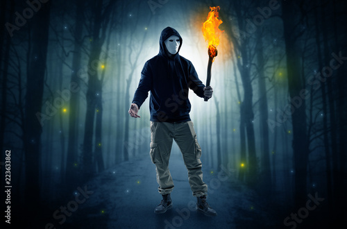 Mysterious man coming from a path in the forest with burning flambeau concept 