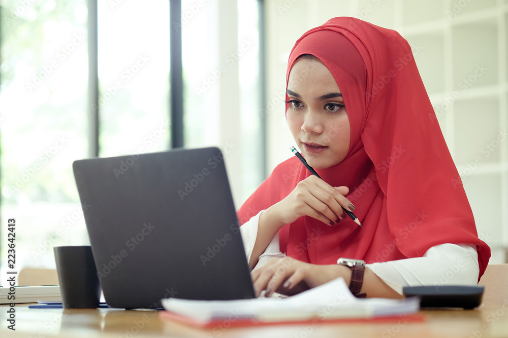Attractive female Arabic working on laptop computer and paperworks on desk Attractive female Arabic working on laptop computer and paperworks on desk