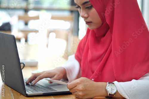 Cropped shot of attractive female Arabic holding credit card and using laptop for shopping or payment online.