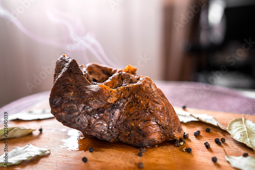 Baked beef shank with spices, close-up on the table, a hot dish with smoke from the oven