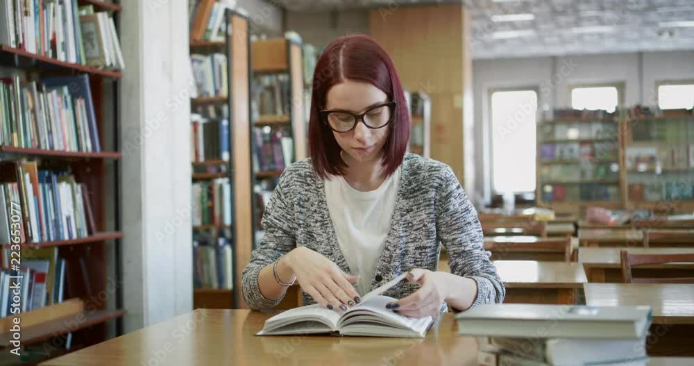 Attractive young woman is reading a book in the reading room of the library. Attractive young woman is reading a book in the reading room of the library.