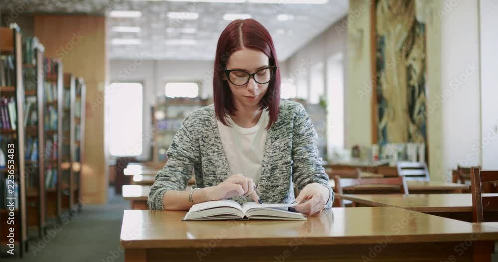 Attractive young woman is reading a book in the reading room of the library. Attractive young woman is reading a book in the reading room of the library.