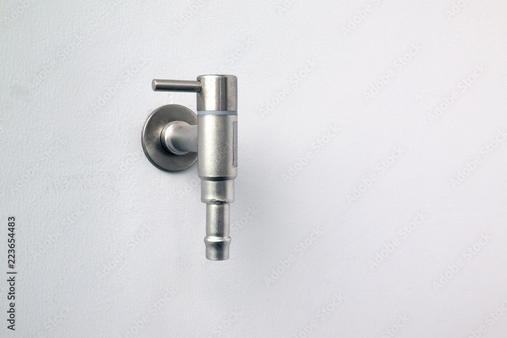 Close up on a silver water tap or tap set up on concrete wall outside of building. Close up on a silver water tap or tap set up on concrete wall outside of building.