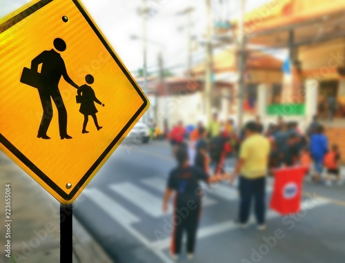 Focus on traffic warning school road sign and blurred background of many students are crossing crosswalk,close up shot and blur background 