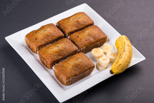 Freshly baked Banana Loaves and banana slices on a white plate and dark table top