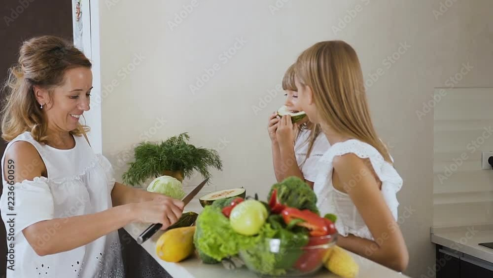 Mother and daughters cutting and eat green melon on the kitchen work surface at home. Woman is cutting a melon and then eat it with her daughters Mother and daughters cutting and eat green melon on the kitchen work surface at home. Woman is cutting a melon and then eat it with her daughters