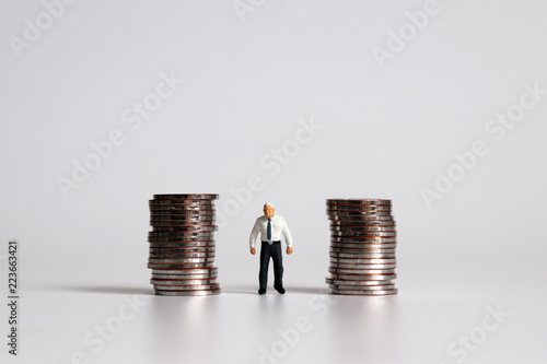 A miniature old man standing among a pile of coins.