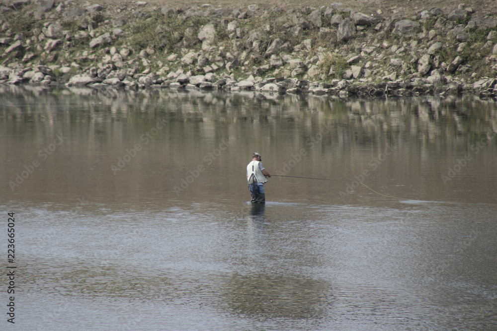 Man is fishing in the river Meuse where it is the border between  Netherlands and Belgium