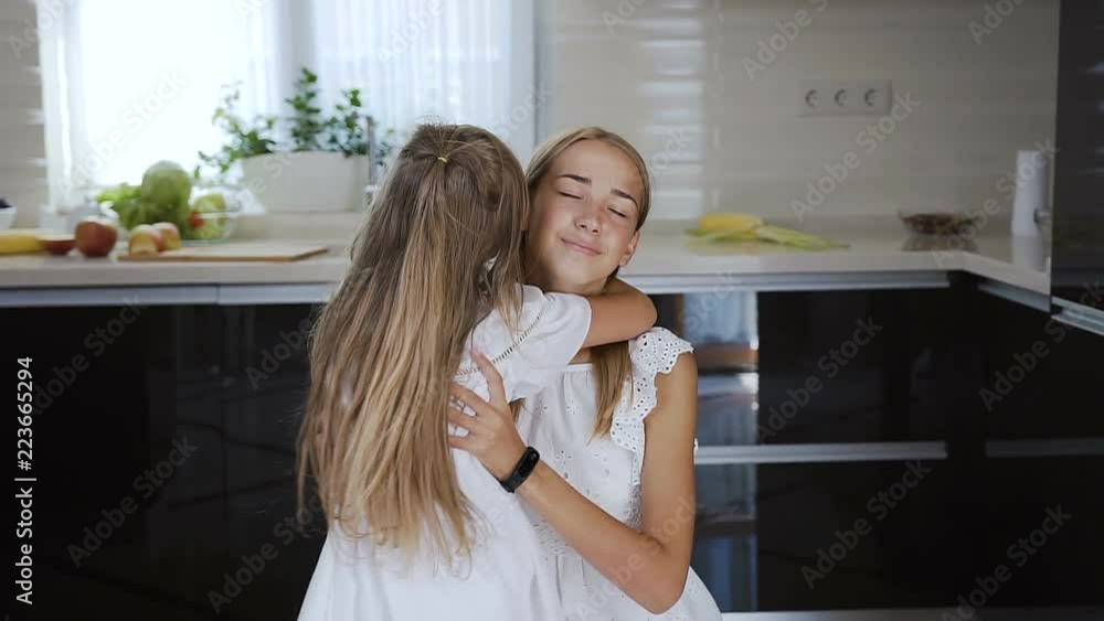 Child running into sister's hands to hug her. Two girls wearing white dress. Little girl happy to meet again in the kitchen with her older sister at home. Girl runs to meet her sister and throws hug Child running into sister's hands to hug her. Two girls wearing white dress. Little girl happy to meet again in the kitchen with her older sister at home. Girl runs to meet her sister and throws hug