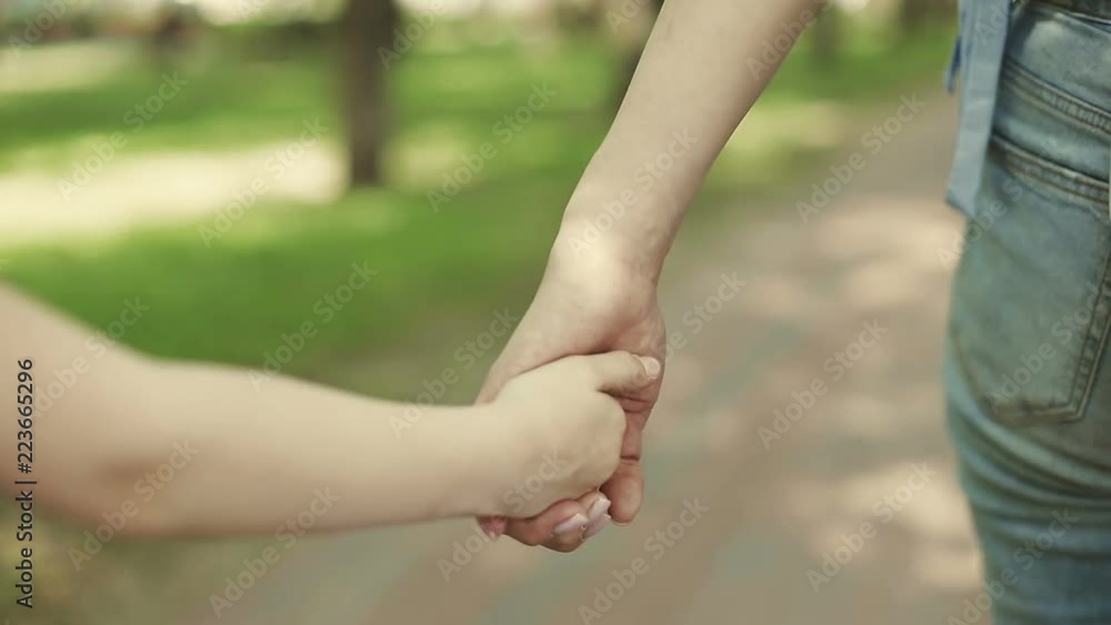 Mother hold the hand of little kid daughter during walking in a park. Mother hold the hand of little kid daughter during walking in a park.