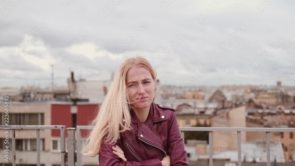 Frozen woman in leather jacket feel cold while standing on the roof in the wind