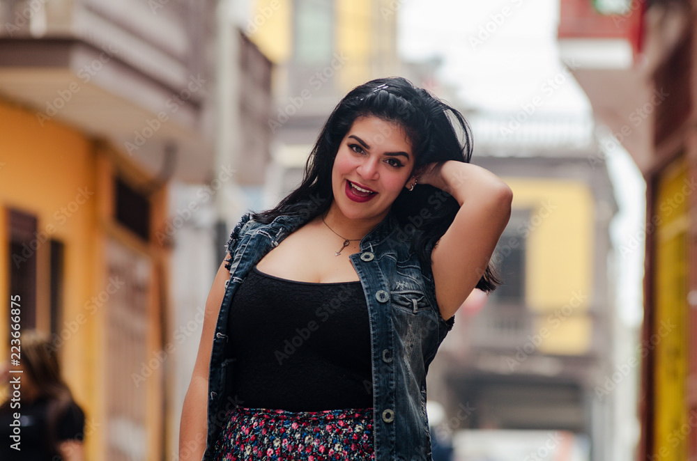 Lifestyle portrait of a beautiful young plus size woman smiling at camera in the city street.