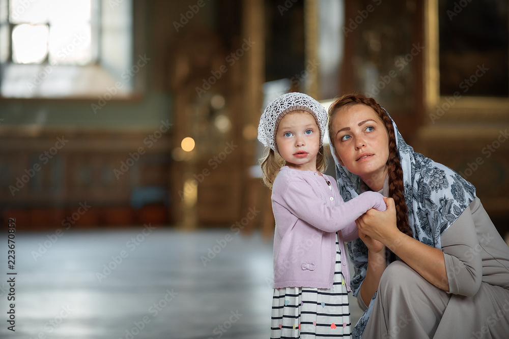 Naklejka premium Young mother and her little blond Caucasian daughter with candles in Orthodox Russian Church
