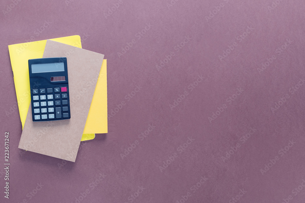 Top view over a school supplies as calculator and notebooks placed from left side of a brown background. Back to school concept. Office supplies flat lay Top view over a school supplies as calculator and notebooks placed from left side of a brown background. Back to school concept. Office supplies flat lay