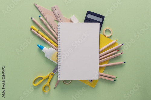 Opened blank notebook over the school supplies such as scissors, rulers, magnificent glass, tapes, calculator, pins, erasor. Back to school and education concept.