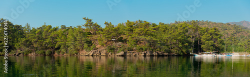 Panoramic view from a bay in Mediterranean with pine trees and the reflection on sea and boats