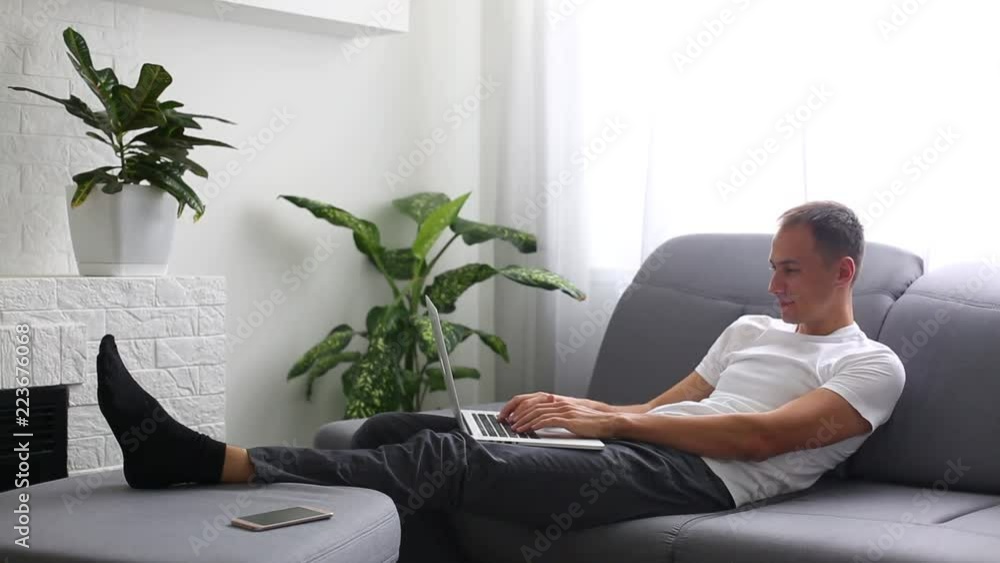 Man using laptop and sitting on the sofa in his flat Man using laptop and sitting on the sofa in his flat