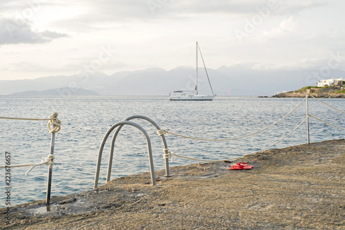 Sea, mountains landscape, sailboat sailing far from seashore. View from concrete pier.
