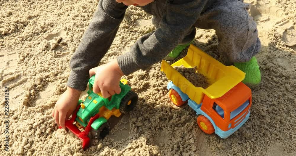 Crop kid playing raod works with toy excavator digs and pours sand into the truck Crop kid playing raod works with toy excavator digs and pours sand into the truck