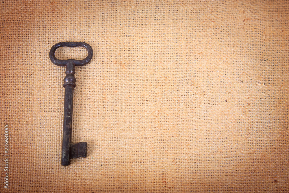 An ancient metal key on the background of sacking. An ancient metal key on the background of sacking.