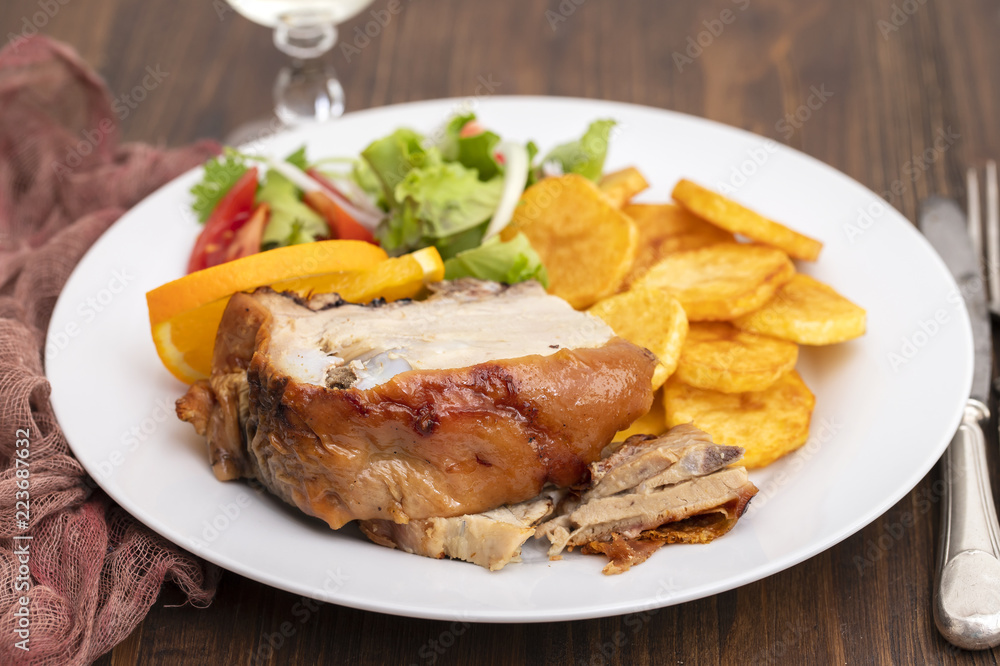 roasted piglet with potato chips and orange on white plate