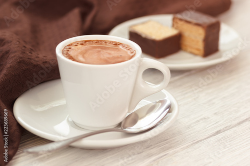 Homemade espresso in white cup with sweets on wooden table with napkin. White wooden table background.